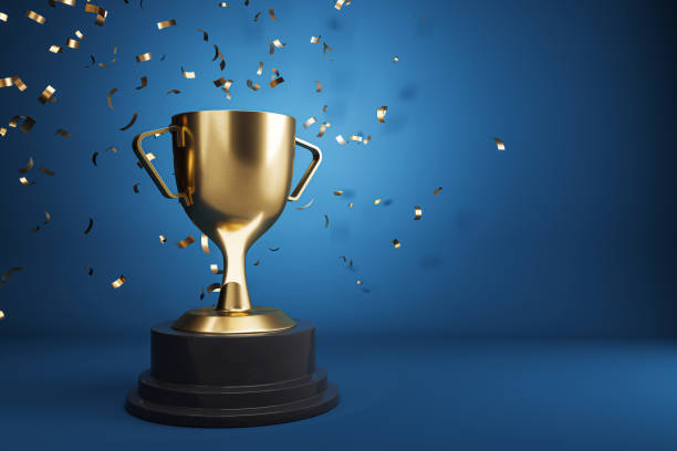 istock A golden trophy on a black pedestal with confetti floating against a blue background, embodying the concept of celebration and victory. 3D Rendering 2160228556