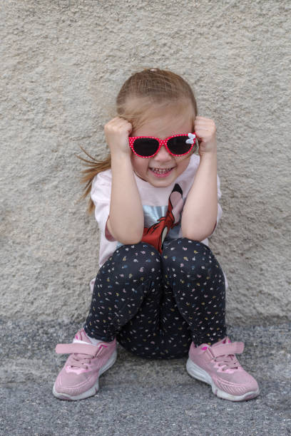 istock Girl sitting against a wall with sunglasses 2160238301