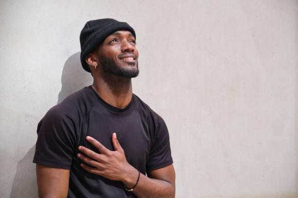 istock Young black man smiling and looking up with hand on chest 2160240355
