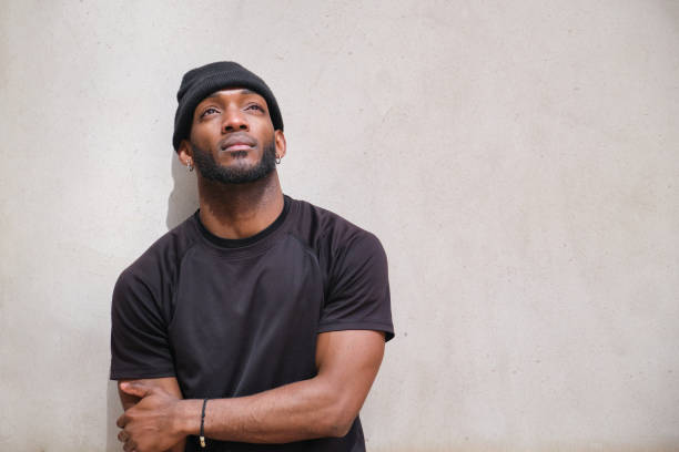 istock Young black man wearing a beanie is looking up with hope 2160240426
