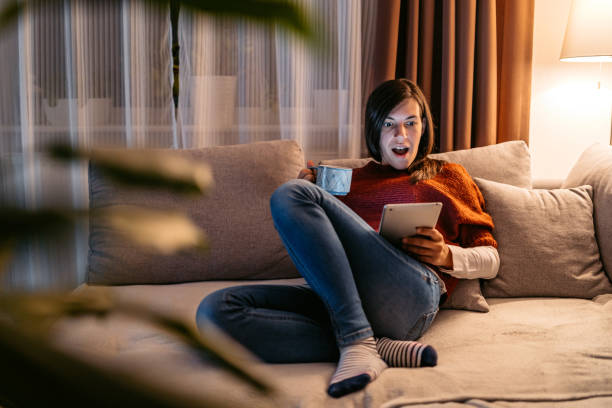 istock Young Woman Being Surprised By Something On A Digital Tablet While Drinking Coffee In The Living Room At Night 2160242804