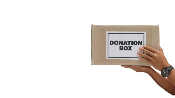A close-up shot of a volunteer's hand holding a cardboard donation box, symbolizing generosity and community support. Isolated on a white background