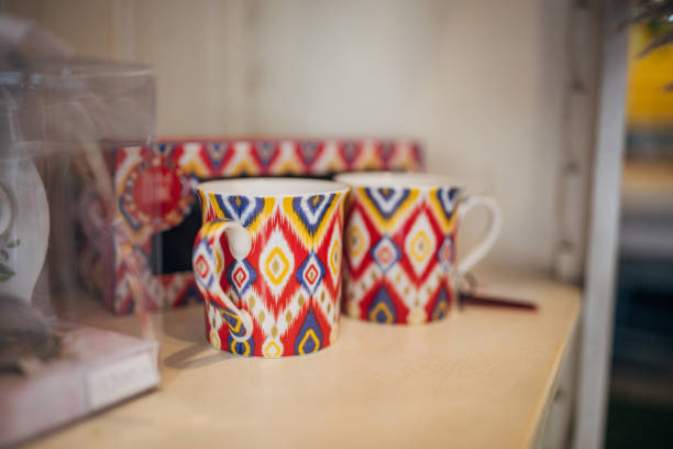 Two colorful mugs featuring geometric patterns are displayed on a wooden shelf, showcasing their vibrant and bold designs, adding a touch of creativity to the interior decor.