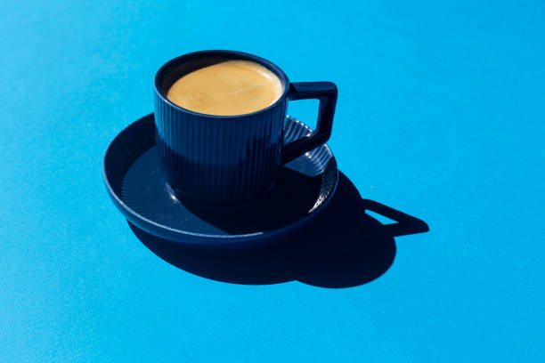 istock A blue cup of coffee with hard shadows on a blue background with copy space. 2160248784
