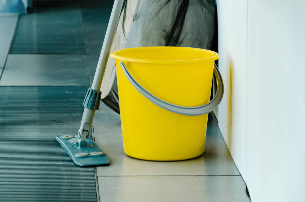 There is a yellow bucket and a mop on the floor, tools for cleaning premises