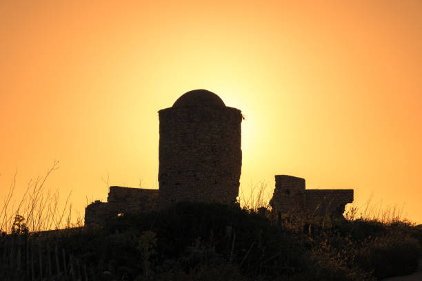 The golden sun sets behind a silhouetted church spire, casting a warm glow over the serene agricultural field.