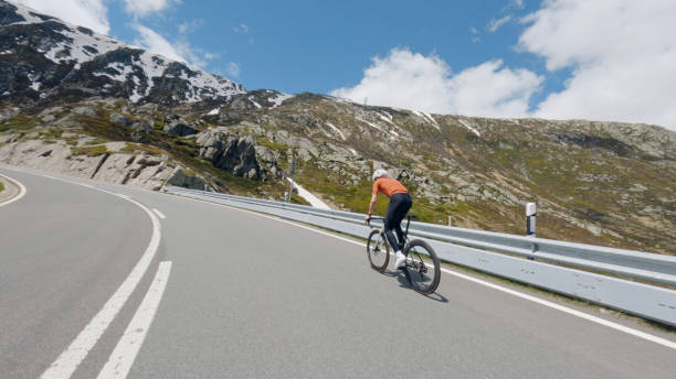 Road biker rides up high mountain pass in springtime