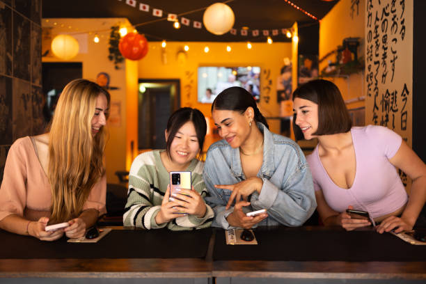 istock Four young women using smartphones at a japanese restaurant 2160262817