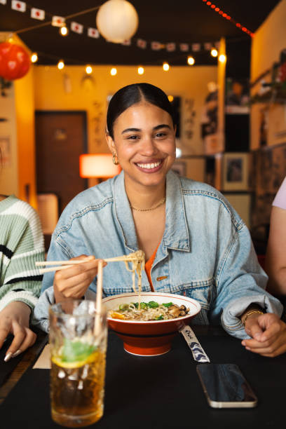 istock Young woman smiling while eating a  bowl of ramen 2160262876