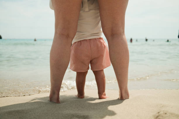 Toddler learning to walk on a sandy beach with the turquoise sea in the background
