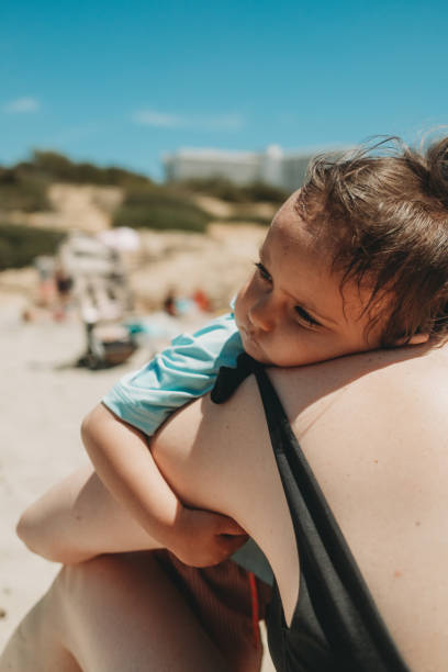 istock Little boy resting on mother's shoulder at the beach on vacation 2160264825