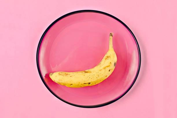 Overripe banana on a pink plate, seen directly above.  Nutritional concept.