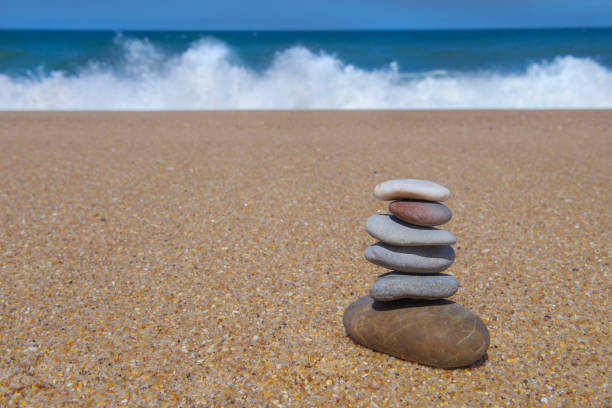 pebbles stacked on a sandy beach in front of ocean and waves background