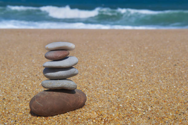 pebbles stacked on a sandy beach in front of ocean and waves background