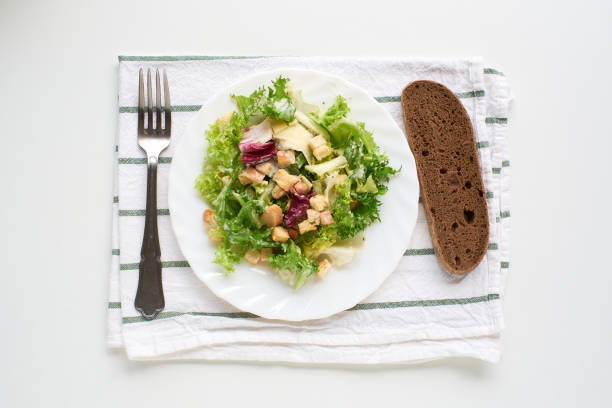 A top down view of a Caesar salad with croutons and bread on a white surface.