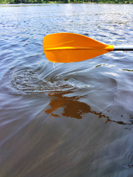 An orange plastic paddle above the water of the river with drops dripping from it. Summer sports and leisure