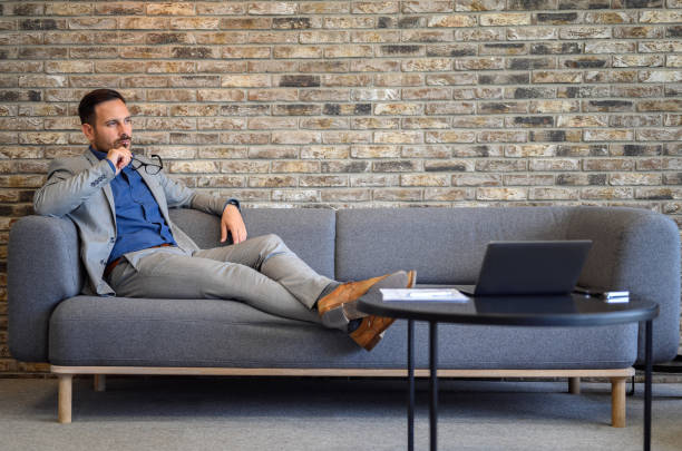 istock Serious young financial advisor holding eyeglasses and thinking while looking away on sofa in office 2160288243