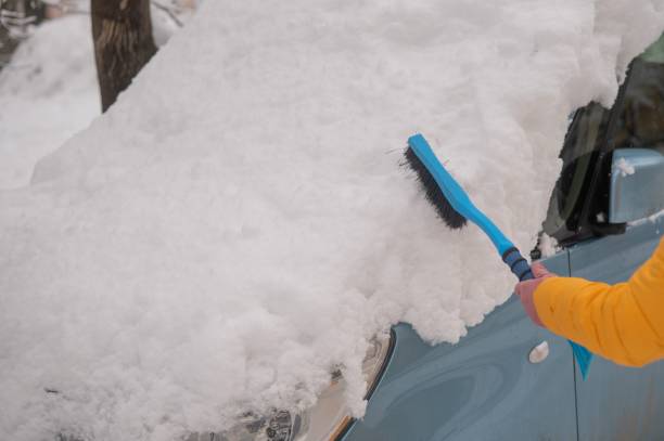 istock Caucasian woman brushing a car from freshly fallen snow. 2160297548