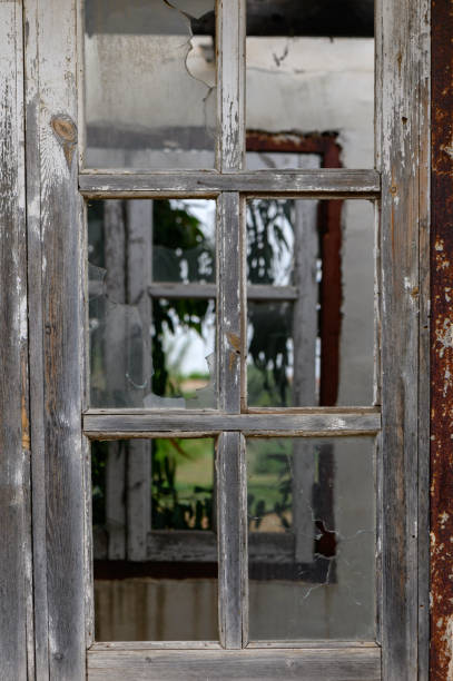 istock Window with broken glass in old building Wooden window frame with partially broken glass in old abandoned brick building 2160301410