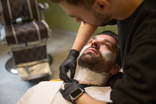 istock High-qualified barber using the straight razor after applying the shaving gel 2160317044
