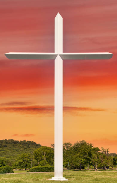 A white Christian cross against a vibrant orange sunset sky.