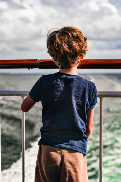 Blond little child is traveling with family by ferry. Schoolboy is enjoying the landscape of the Adriatic Sea. Cruise ship vacation during the holidays.