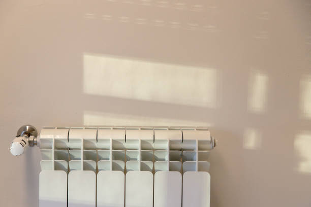 istock Warm sunlight filters through a window, casting soft shadows on a wall above a white radiator, creating a serene and cozy indoor atmosphere. 2160324323