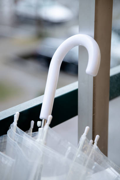 A clear umbrella with a white handle rests against a window, capturing the serene ambiance of a rainy day and the delicate balance of indoor and outdoor elements.