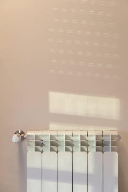 istock Warm sunlight filters through a window, casting soft shadows on a wall above a white radiator, creating a serene and cozy indoor atmosphere. 2160324344
