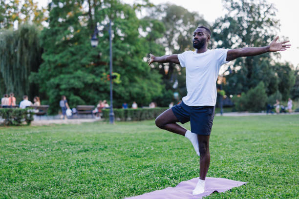 istock Man practicing yoga in tree pose in a green park. 2160325511