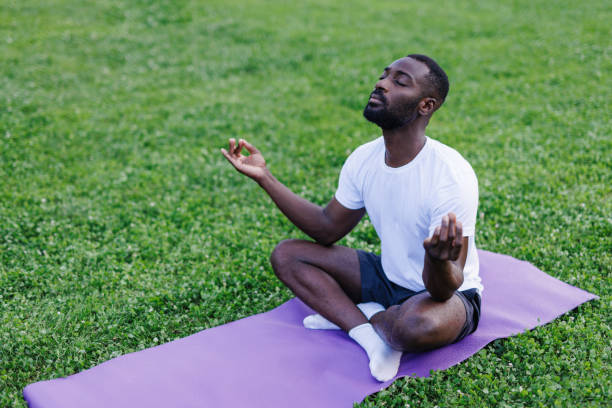 istock Man seated cross-legged, meditating on yoga mat outdoors 2160325607