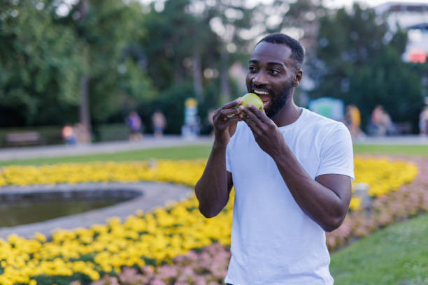 istock Man eating a green apple in a vibrant public park. 2160326638