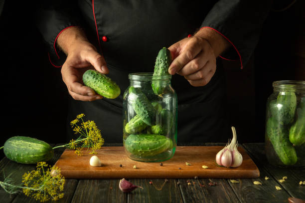 istock Chef hands filling jar with cucumbers before canning with spices on kitchen table. Concept of pickling tasty cucumber 2160328060