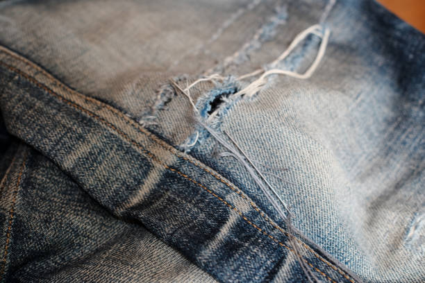 A needle and thread sew up a hole in a denim. Work of a seamstress or tailor with a needle, garment industrial concept.