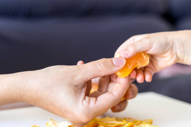 istock Adult's hand offering tangerine to a child 2160344263