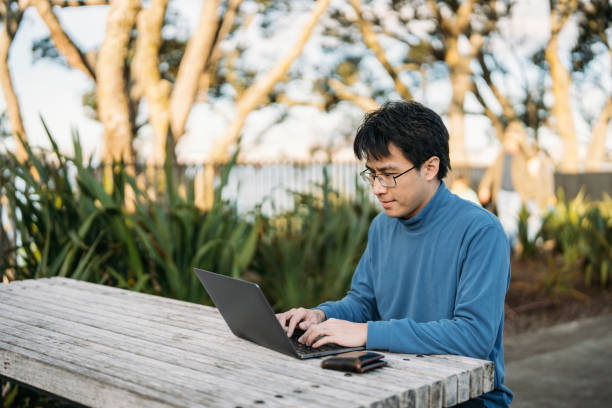 istock Young man typing on his laptop in a park with his wallet by the side 2160352302