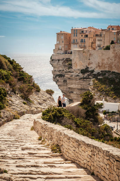 Bonifacio, Corsica, France - 28th May 2024: A young couple ascend the stone steps in front of the citadel of Bonifacio perched on cliffs above the Mediterranean sea on the island of Corsica