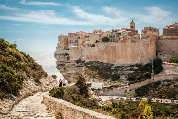 Bonifacio, Corsica, France - 28th May 2024: A young couple ascend the stone steps in front of the citadel of Bonifacio perched on cliffs above the Mediterranean sea on the island of Corsica