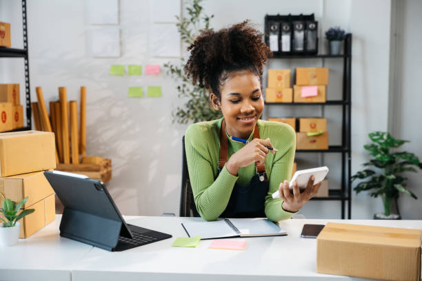 istock African Owner SME Small and Medium Enterprises woman received orders from clients and check profit on calculator preparing products in parcel cardboard box packaging at home ready for delivery 2160368074