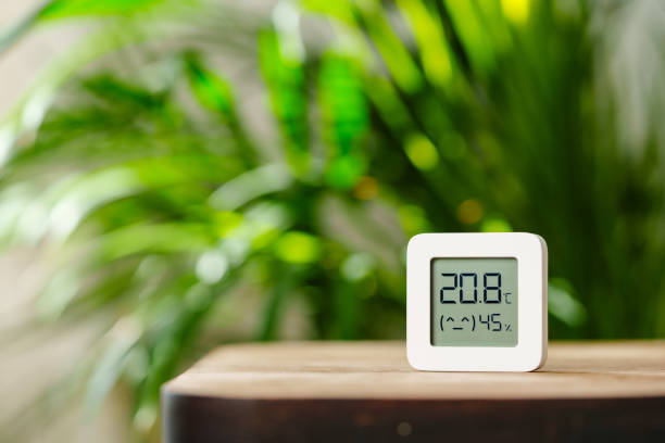 istock White Digital Thermometer Displaying Temperature and Humidity on Wooden Table With Green Plant in Background 2160386215