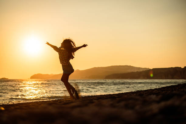 Playful woman having fun while spinning with her arms outstretched on the beach at sunset. Copy space.