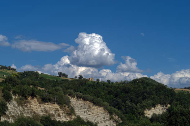 forested hills and layered rock formations under sky with cumulus clouds