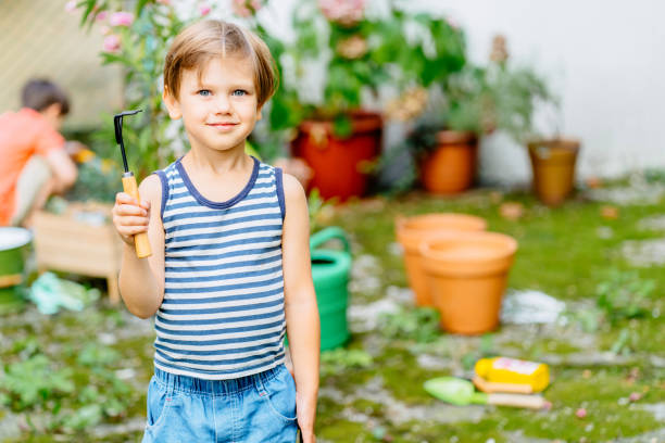 Two children boy working at backyard. Brother with gardening tools spending time, playing, create cozy courtyard together outdoor at beautiful summer day.Developmental activities for children concept.
