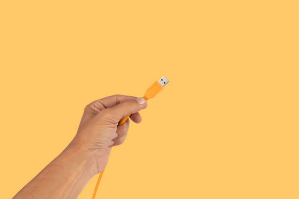 Male hand holding an orange usb cable isolated on yellow background. High quality photo