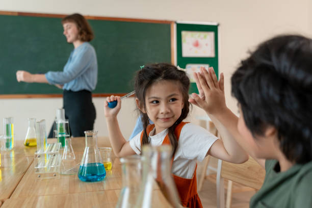 istock Adorable student learn with teacher in classroom at elementary school. Group of young schoolboy and girl sit on table, study science and doing chemistry experiment with fun activity at kindergarten. 2160415459