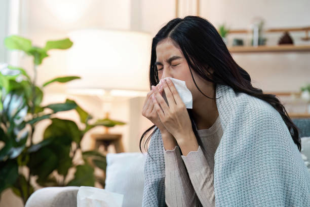 istock Young Woman Sneezing into Tissue While Wrapped in Blanket at Home, Battling Cold and Flu Symptoms 2160417032