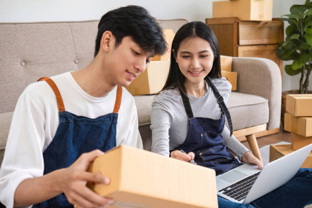 istock Young Couple Selling Items Online from Home, Packing Boxes and Using Laptop for E-commerce Business 2160418061