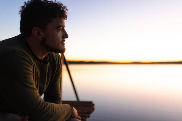 Young man standing by the lake in sunset