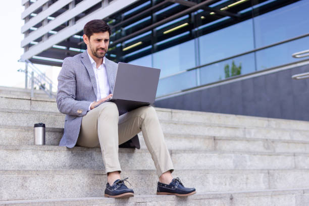 istock Businessman working on laptop sitting on steps in city 2160421902