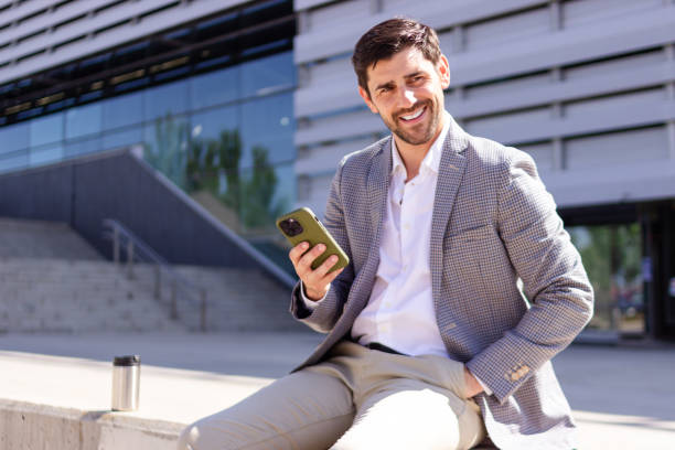 istock Handsome businessman sitting outside office building using smartphone 2160421987